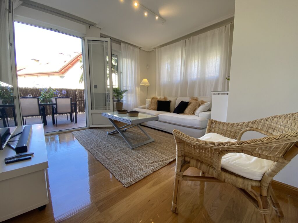 Salón luminoso con sofá blanco, mesa de centro y sillón de mimbre