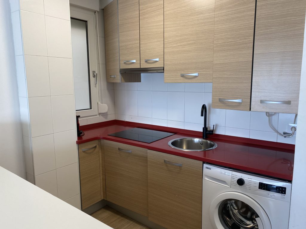 Cocina con encimera roja, placa de inducción, fregadero y lavadora