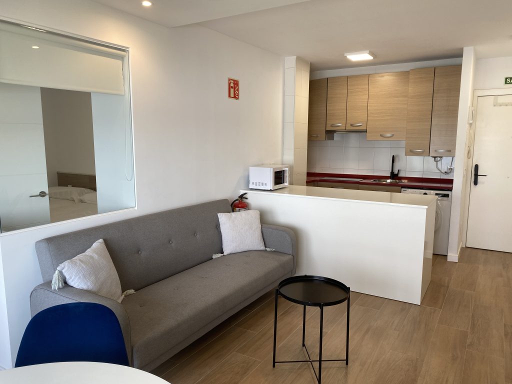 Salón con sofá gris, mesa auxiliar y cocina americana al fondo