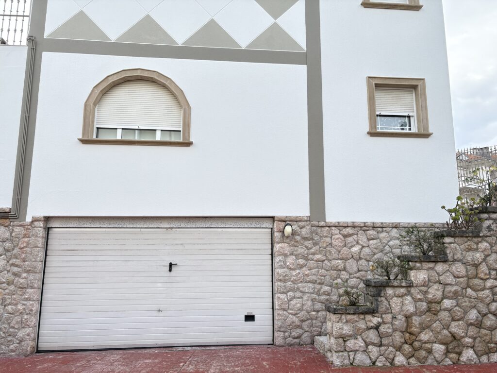 Fachada de casa con garaje blanco y muro de piedra.