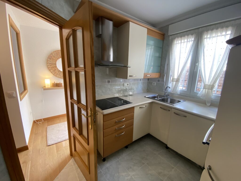 Cocina luminosa con armarios de madera y ventana con cortinas.