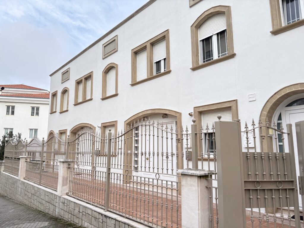 Edificio blanco con ventanas enmarcadas y valla metálica decorativa.