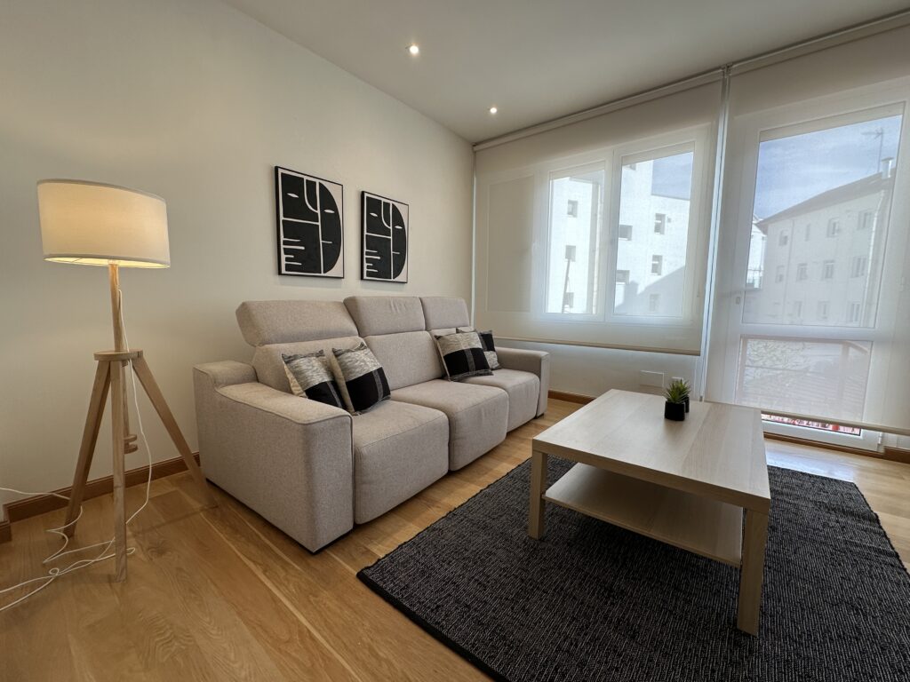 Salón moderno con sofá beige, lámpara de trípode y alfombra.