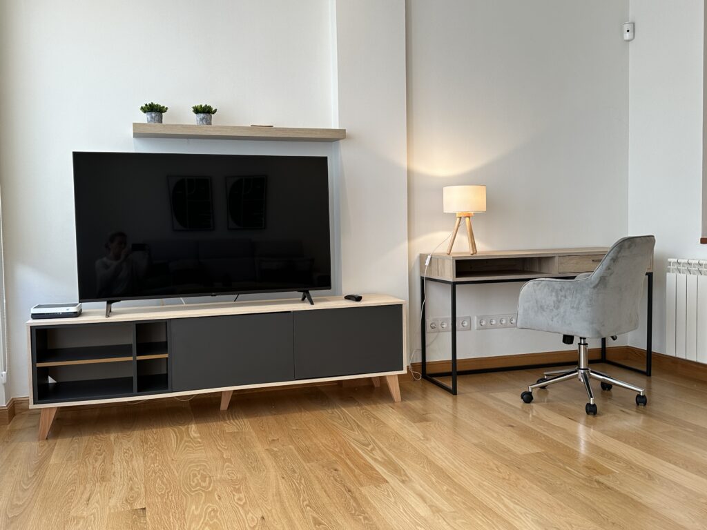 Salón moderno con televisor, escritorio de madera y silla gris.