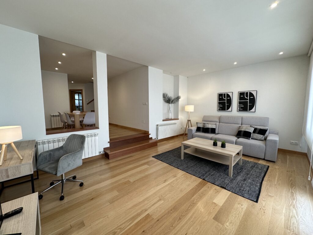 Salón moderno con sofá gris, mesa de madera y despacho.