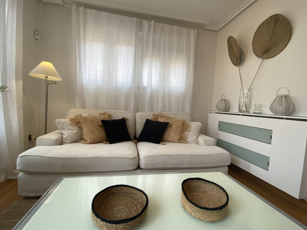 Salón con sofá beige, cojines y mueble bajo blanco con decoración