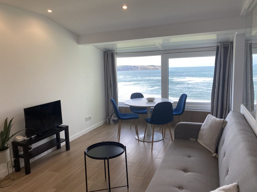 Salón con sofá, televisión y mesa de comedor con vistas al mar