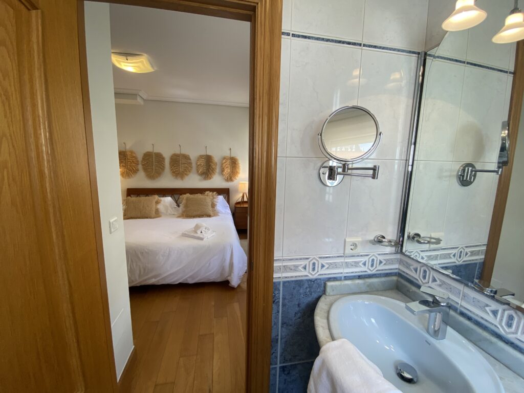 Baño moderno con vista a un dormitorio con cama doble.