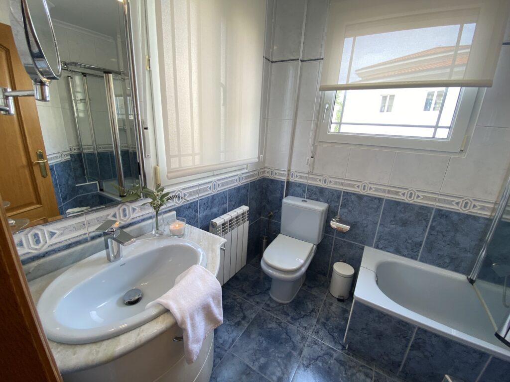 Baño clásico con azulejos azules, lavabo blanco y bañera.