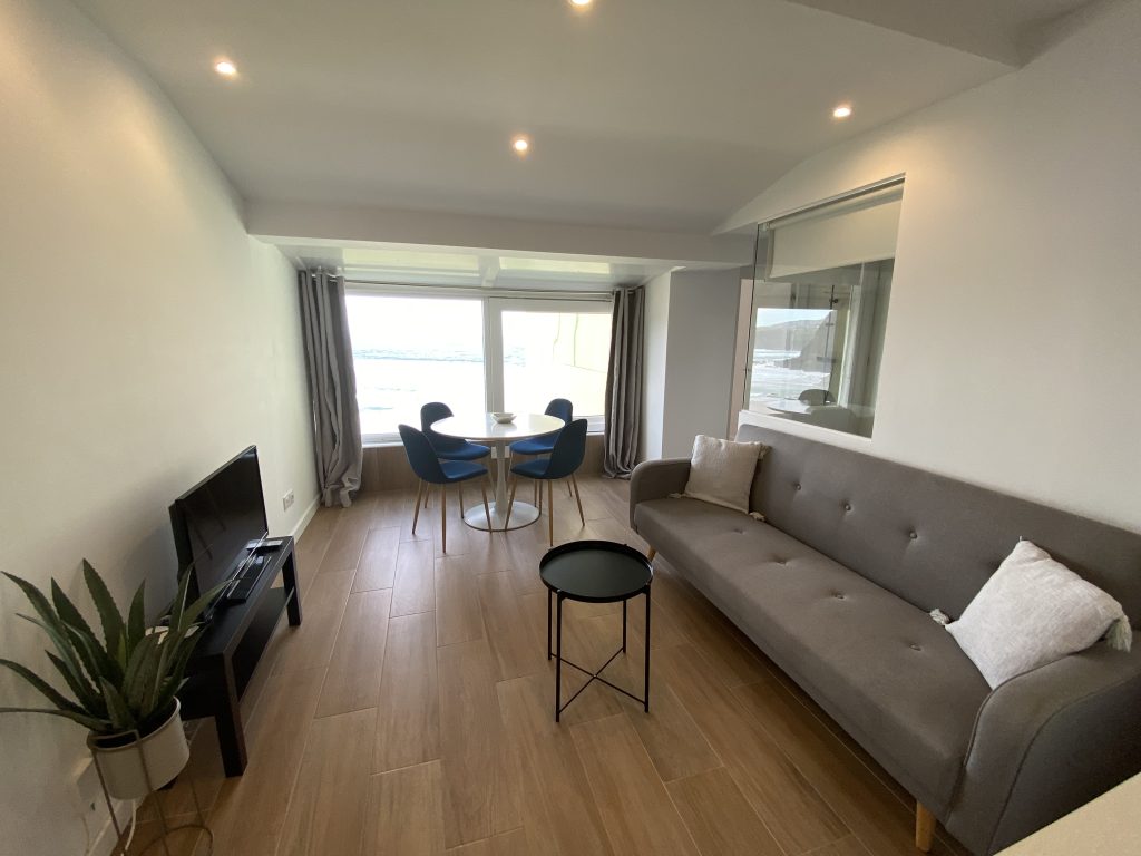 Salón con sofá gris, mesa auxiliar y mesa de comedor junto al ventanal
