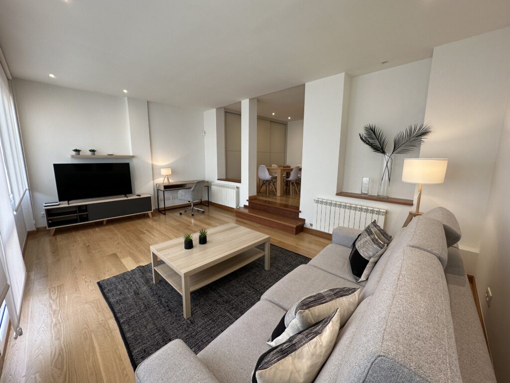 Salón moderno con sofá gris, mesa madera y televisión.