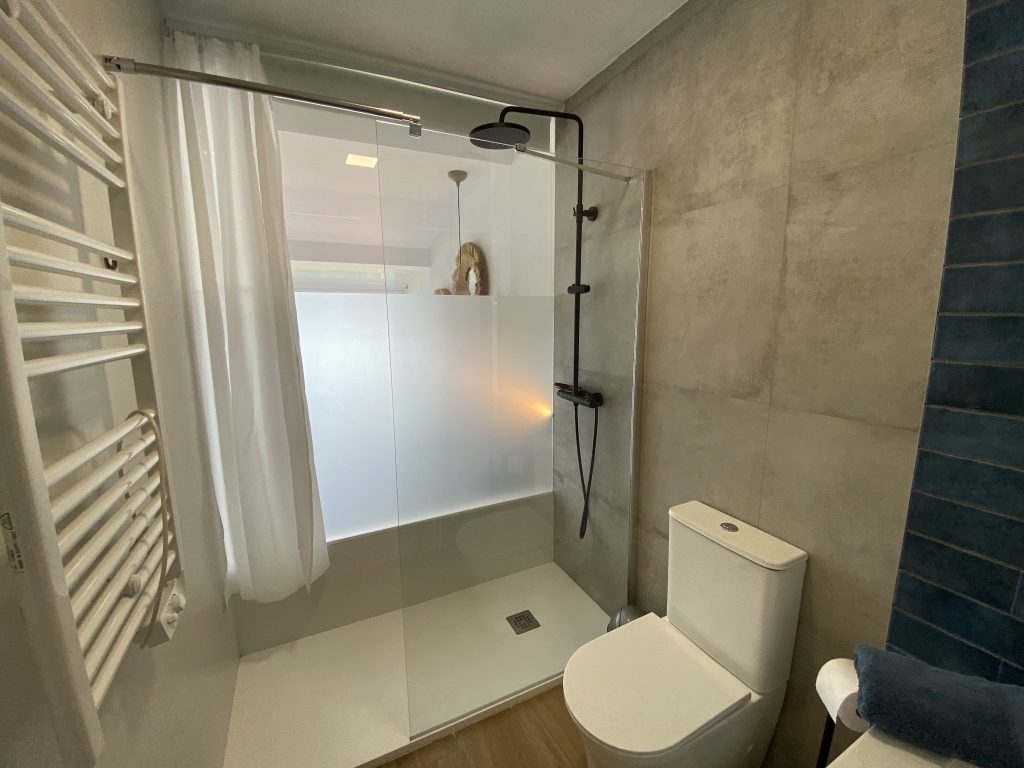 Baño con ducha de obra, mampara de cristal y toallero