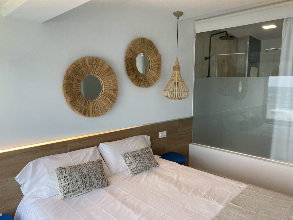 Dormitorio con cama doble, espejos decorativos y lámpara de fibra natural