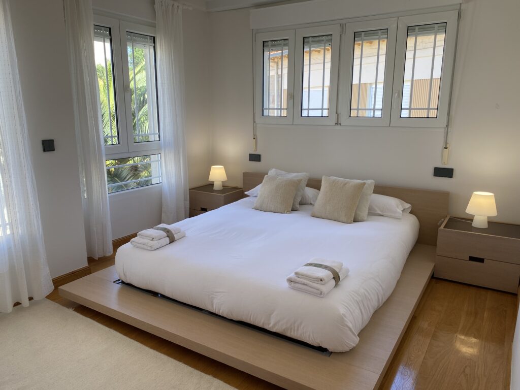 Dormitorio con cama doble sobre tarima elevada y ventanas a ambos lados