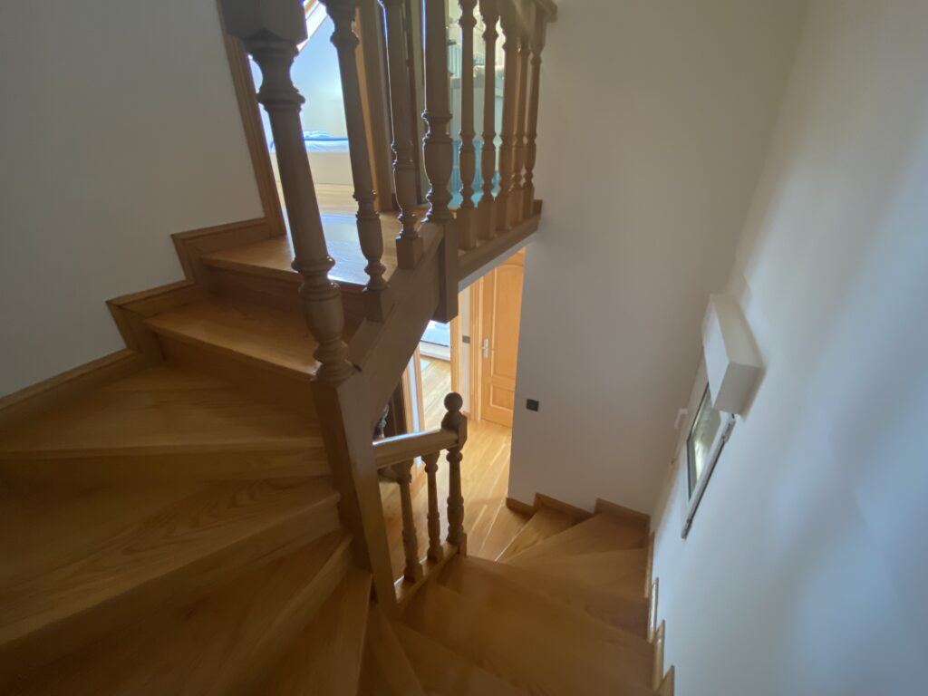 Escalera de madera con barandilla torneada hacia la planta inferior