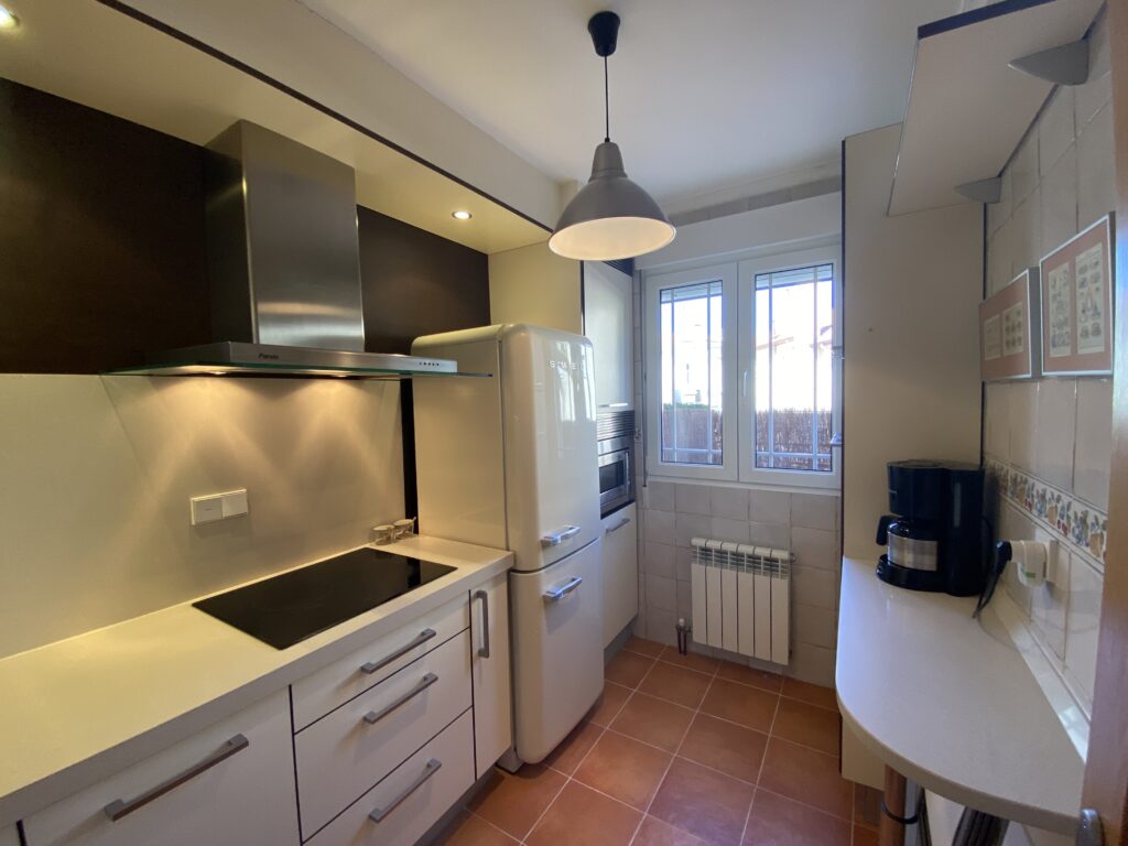 Cocina en blanco con campana de acero, vitrocerámica y cafetera