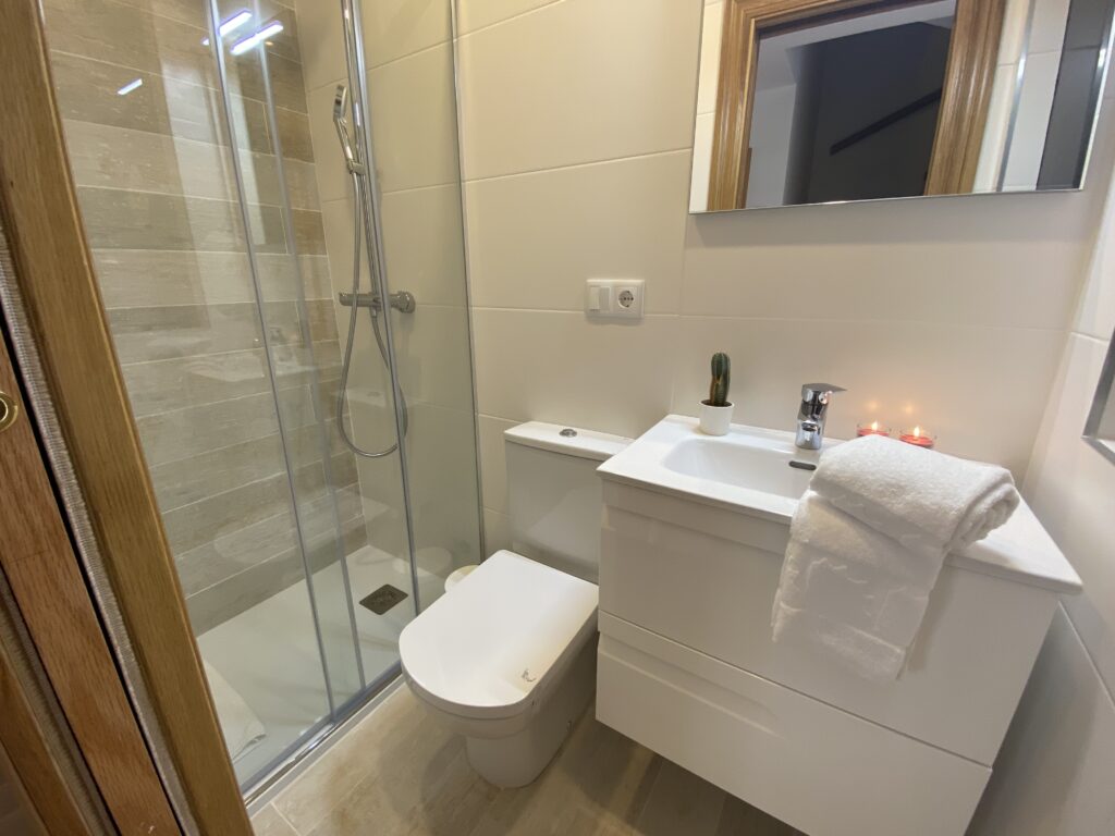 Baño moderno con ducha de cristal y mobiliario blanco.