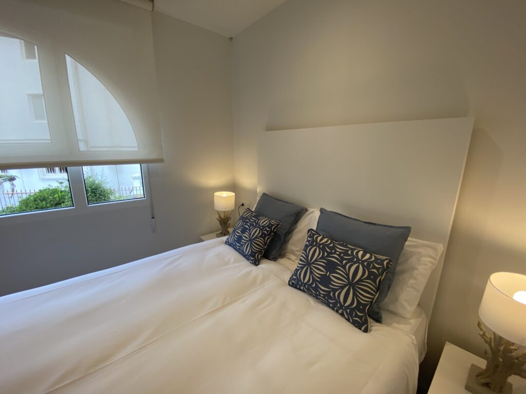 Dormitorio moderno con cama blanca, cojines azules y lámparas encendidas