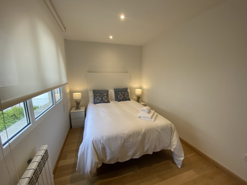 Dormitorio moderno con cama doble, sábanas blancas y lámparas auxiliares.